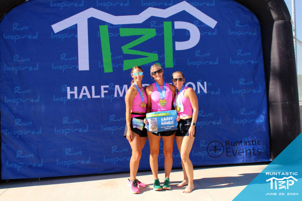 3 runners holding up a sign in front of a Runtastic TIMP photo backdrop in American Fork, Utah.